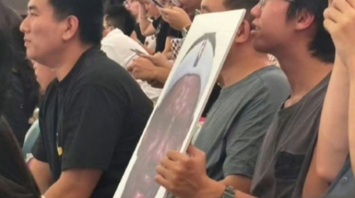 詹姆斯中国行成都活动现场 一球迷拿着詹姆斯经典哭脸照坐在场边